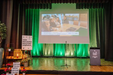 Valmiera, Letonya - 24 Nisan 2025 - Konferans. Letonya 'da sürdürülebilirlik temalı bir öğrenci iş projesi için yeşil ışıklandırma, sunum ekranı ve ödül tabelalarıyla sahne kurulumu.