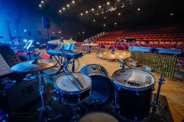 Valmiera, Letonya - 8 Mayıs 2025 - Çanlar, mikrofonlar ve klavyeli bir konser salonunda davul seti, boş kırmızı oditoryum koltuklarının önünde canlı performans için hazırlandı.