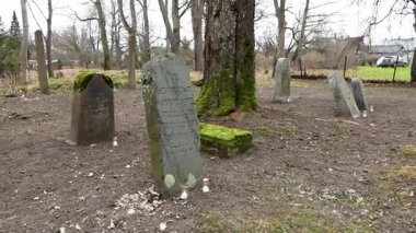 Cesis, Letonya - Ekim 12, 2024 - Eski yosun kaplı mezar taşları İbranice yazıtlar ve anıt mumlar ile sonbaharın sonlarında sessiz, ağaçlık bir Yahudi mezarlığında.
