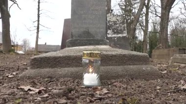 Cesis, Letonya - 12 Ekim 2024 - Arka planda Ella Kussmann 'ın mezar taşı bulunan bir Yahudi mezarlığındaki bir mezara yerleştirilmiş cam bir kavanozda anıt mum yanar..
