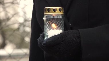 Cesis, Letonya - Ekim 12, 2024 - Siyah eldivenli ve ceketli bir kişinin cam bir kavanozda yanan bir mum, arka planda bulanık bir çitle ve ağaçlarla yakın çekimi.