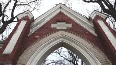 Cesis, Letonya - Ekim 12, 2024 - Arka planda çıplak ağaçlar bulunan CSI, Letonya 'daki bir mezarlığa veya anıta Gotik tarzı tuğla kemerli giriş.