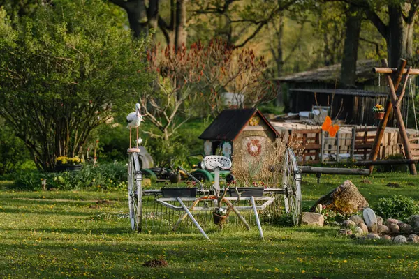 Smiltene, Letonya - 17 Mayıs 2025 Metal bir bahçe dekoru, traktör koltuğu, tekerlekler, asma kaplar ve yemyeşil ve çiçeklerle dolu yemyeşil bir bahçede leylek figürü.