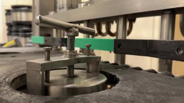 Endüstriyel ekipmanların mekanik metal klemp bileşenlerine yakın çekim, bir üretim hattı ile çevrili ve arka planda bulanık variller.