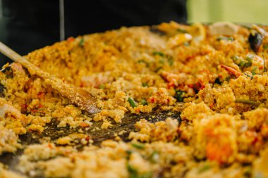 Kalan pirinç, deniz ürünleri ve sebzelerle ahşap bir spatulayla temizlenmiş neredeyse boş bir paella tavasına yakın plan..