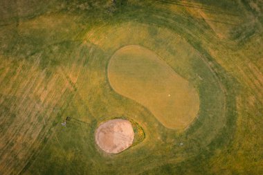 Valmiera, Letonya - 21 Mayıs 2025 Kum sığınağı ve iki oyunculu golf sahasının havadan görünüşü, biçilmiş çim biçme yerleri ve altın akşam ışığı desenleri.