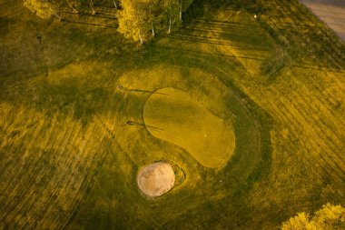 Valmiera, Letonya - 21 Mayıs 2025 - Gün batımında golf yeşil ve kum sığınağının havadan görünüşü.
