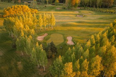 Valmiera, Letonya - 21 Mayıs 2025 - Çevresi altın saatinde canlı ağaçlarla çevrili golf sahasının havadan görünüşü kırsal alana doğru uzanan çim alanları.