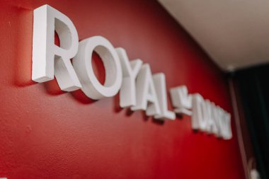 Valmiera, Latvai - 23 Mayıs 2025 - Bir berber dükkanı veya kuaför salonu içinde muhtemelen kırmızı iç duvarda ROYAL DANDY monte beyaz 3D işareti yakın çekim