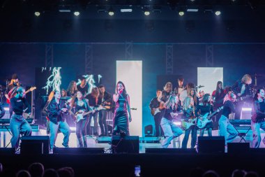 Valmiera, Letonya - 22 Mayıs 2025 - Siyah elbiseli kadın solist, Yamaha enstrümanlarının yer aldığı renkli, yüksek enerjili bir konserde dansçılar ve orkestrayla birlikte sahneye çıktı..