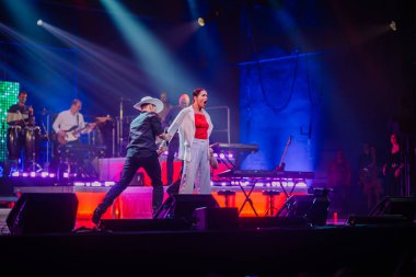 Valmiera, Letonya - 22 Mayıs 2025 - Erkek bir dansçının Yamaha sponsorluğundaki canlı konser performansı sırasında beyazlar içinde şaşırmış bir kadın şarkıcıyı canlandırdığı dramatik sahne anı.