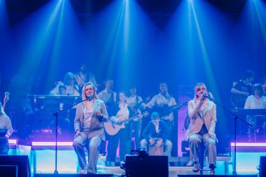 Valmiera, Letonya - 22 Mayıs 2025 - İki kadın şarkıcı, Yamaha enstrümanlı bir grup tarafından desteklenen, mavi ışığın altında bir konser sırasında sahne aldılar..
