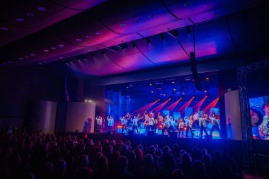 Valmiera, Letonya - 22 Mayıs 2025 - Dinamik ışıklandırma, dansçılar ve müzisyenlerle dolu kalabalık bir konser salonunun geniş görünümü Yamaha enstrümanları kullanarak, canlı bir performans yaratıyor.