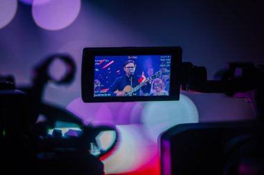 Valmiera, Letonya - 22 Mayıs 2025 - Yamaha enstrümanları ve renkli ışıklarla sahnede bir erkek gitarist ve şarkıcıyı çeken kamera görüntüsü.
