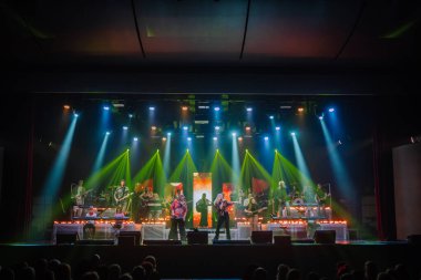 Valmiera, Letonya - 22 Mayıs 2025 - Canlı seyirci önünde Yamaha klavye ve enstrümanları kullanarak, renkli ışıklar altında vokalistler ve grupla tam sahne konser performansı.