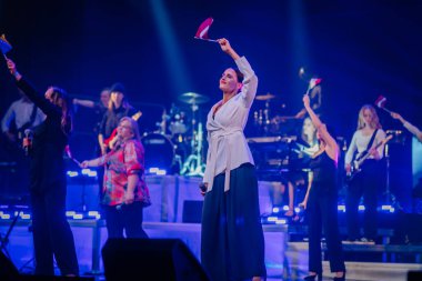 Valmiera, Letonya - 22 Mayıs 2025 - Sahnede Yamaha davulları ve klavyelerinin olduğu bir konser sırasında, canlı ışıklandırma ve müzikal atmosfer altında göstericiler bayrak sallıyor.