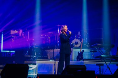 Valmiera, Letonya - 22 Mayıs 2025 - Bir konser sırasında sahne arkasında Yamaha klavyesi ve müzik aletleri ile mavi ışık altında şarkı söyleyen kadın sanatçı.