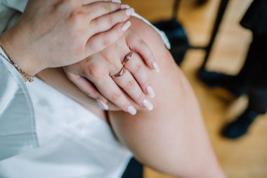 Bir kadının ellerini dizinde dinlendirirken, zarif çıplak manikür, altın yüzükler ve bilezik sergiliyor, muhtemelen düğün hazırlıkları sırasında.