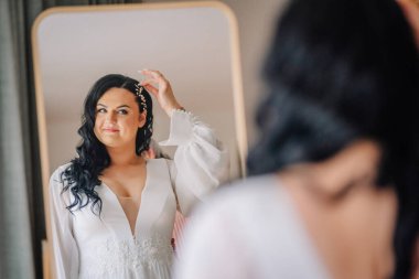 Valmiera, Latvai - 23 Mayıs 2025 - Gelin aynaya bakarken saçını düzeltir, çiçekli beyaz bir gelinlik giyer, özel gününe hazırlanır..