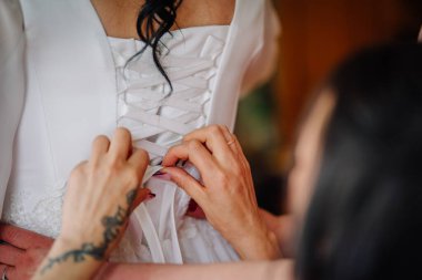 Valmiera, Latvai - 23 Mayıs 2025 - Beyaz gelinliğin bağcıklarını sıkan eller, gelini seremonisi için sıcak ve samimi bir şekilde hazırlıyor..