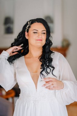 Beyaz elbiseli, kendine güvenen gelin saçlarına dokunuyor, bukleli saçlarıyla ve narin kolyesiyle, düğün günü içinde zarafet saçıyor..