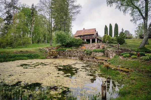 Etrafı yemyeşil, taştan teraslarla çevrili kırsal bir kır evi ve sakin bir ilkbahar ortamında su bitkileriyle dolu doğal bir gölet..