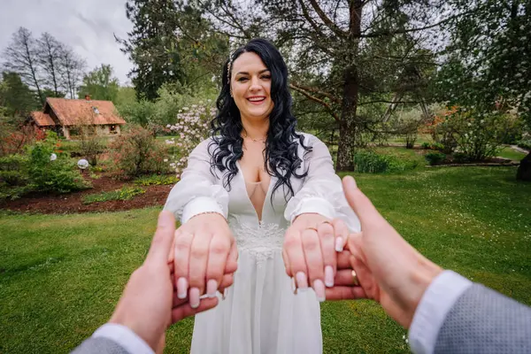 Beyaz elbiseli, gülümseyen gelin, damatların elini tutmak için uzanır. Çiçekli bir bahçede, düğün günlerinde sevgi, neşe ve bağ uyandırır.