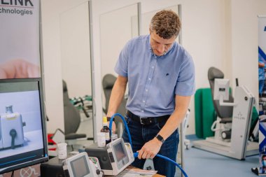Valmiera, Letonya - 31 Mayıs 2025 - Mavi gömlekli adam tıbbi eğitim sırasında ekranlar ve klinik ekipmanlarla çevrili solunum cihazı bağlantısını gösteriyor.