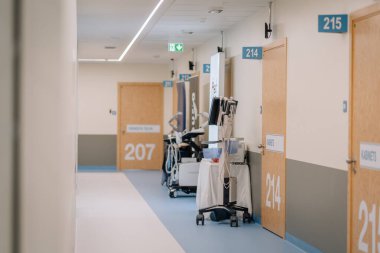 Valmiera, Letonya - 31 Mayıs 2025 - Temiz ve modern hastane koridoru numaralandırılmış ahşap kapılar, tekerlekli sandalyelerde teşhis ekipmanları ve klinik bir çevrede tabela.
