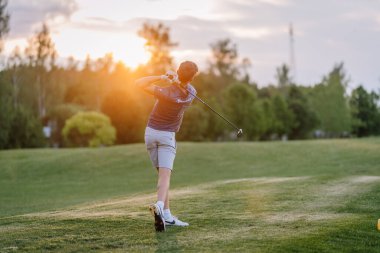 Valmiera, Letonya - 10 Haziran 2025 - Golfçü, yemyeşil ve ılık ışıklarla çevrili yemyeşil bir golf sahasında gün batımında bir salıncağı bitirir..