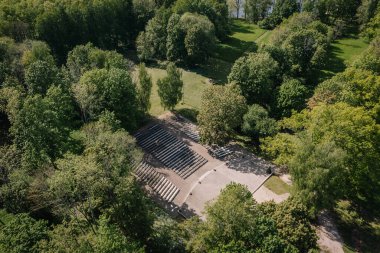 Koknese, Letonya - 27 Mayıs 2025 - Yeşillik yeşil ağaçlar ve açık park alanlarıyla çevrili bir açık hava amfi tiyatrosu, katmanlı oturma ve açık sahne alanı.
