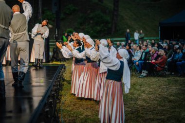 Valmiera, Letonya - 7 Haziran 2025 - Geleneksel Letonyalı kostümlü kadınlar GAUJA 80 halk festivali sırasında sahnede ponpon kız dansçıları.