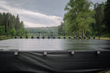 Valmiera, Letonya - 7 Haziran 2025 - Manzaralı orman ve nehirle çevrili boş bir sahne, yağmurdan sonra ıslak, GAUJA 80 gösterisine hazır, sahne ışıkları harekete hazır..