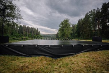 Valmiera, Letonya - 7 Haziran 2025 - GAUJA 80 kültürel etkinliğinde fırtınalı gökyüzünün altında, aydınlatma ekipmanlarıyla donatılmış ıslak bir açık hava sahnesi.