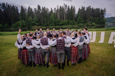 Valmiera, Letonya - 7 Haziran 2025 - Geleneksel giyinmiş Letonyalı halk dansçıları GAUJA 80 'de nehir kenarında bir çember oluşturarak, doğadaki birlik ve mirası kutluyorlar..