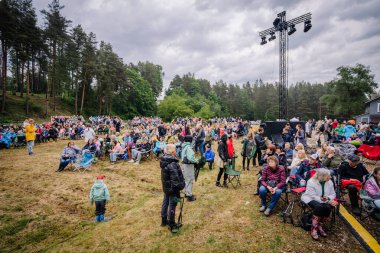 Valmiera, Letonya - 7 Haziran 2025 - Büyük bir kalabalık, pek çoğu katlanan sandalyelerde, bulutlu gökyüzünün altında sıcak bir şekilde giyinmiş bir şekilde açık hava orman etkinliğinde toplandı. Festival topluluğu toplanıyor.
