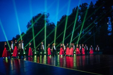 Valmiera, Letonya - 7 Haziran 2025 - GAUJA 80 'deki geleneksel Letonya halk dansları kolajı, renkli kostümlü dansçıları gece aydınlatmalı bir sahnede sergiliyorlar..