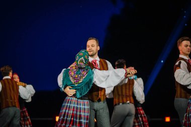 Valmiera, Letonya - 7 Haziran 2025 - GAUJA 80 'deki geleneksel Letonya halk dansları kolajı, renkli kostümlü dansçıları gece aydınlatmalı bir sahnede sergiliyorlar..