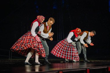 Valmiera, Letonya - 7 Haziran 2025 - GAUJA 80 'deki geleneksel Letonya halk dansları kolajı, renkli kostümlü dansçıları gece aydınlatmalı bir sahnede sergiliyorlar..