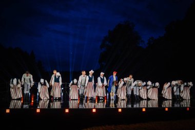 Valmiera, Letonya - 7 Haziran 2025 - GAUJA 80 'deki geleneksel Letonya halk dansları kolajı, renkli kostümlü dansçıları gece aydınlatmalı bir sahnede sergiliyorlar..