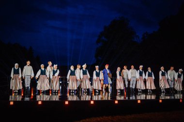 Valmiera, Letonya - 7 Haziran 2025 - GAUJA 80 'deki geleneksel Letonya halk dansları kolajı, renkli kostümlü dansçıları gece aydınlatmalı bir sahnede sergiliyorlar..