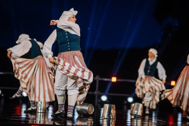 Valmiera, Letonya - 7 Haziran 2025 - GAUJA 80 'deki geleneksel Letonya halk dansları kolajı, renkli kostümlü dansçıları gece aydınlatmalı bir sahnede sergiliyorlar..