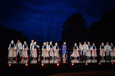 Valmiera, Letonya - 7 Haziran 2025 - GAUJA 80 'deki geleneksel Letonya halk dansları kolajı, renkli kostümlü dansçıları gece aydınlatmalı bir sahnede sergiliyorlar..