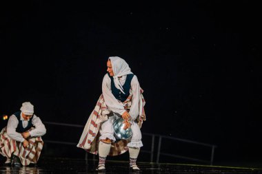 Valmiera, Letonya - 7 Haziran 2025 - GAUJA 80 'deki geleneksel Letonya halk dansları kolajı, renkli kostümlü dansçıları gece aydınlatmalı bir sahnede sergiliyorlar..