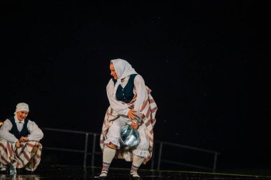 Valmiera, Letonya - 7 Haziran 2025 - GAUJA 80 'deki geleneksel Letonya halk dansları kolajı, renkli kostümlü dansçıları gece aydınlatmalı bir sahnede sergiliyorlar..