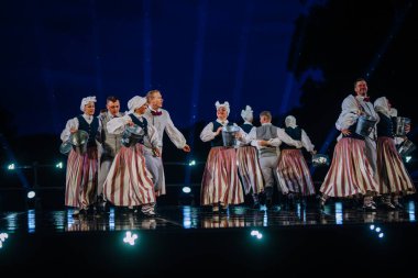 Valmiera, Letonya - 7 Haziran 2025 - GAUJA 80 'deki geleneksel Letonya halk dansları kolajı, renkli kostümlü dansçıları gece aydınlatmalı bir sahnede sergiliyorlar..
