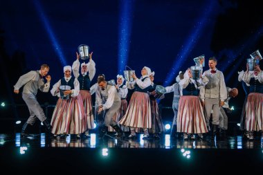 Valmiera, Letonya - 7 Haziran 2025 - GAUJA 80 'deki geleneksel Letonya halk dansları kolajı, renkli kostümlü dansçıları gece aydınlatmalı bir sahnede sergiliyorlar..