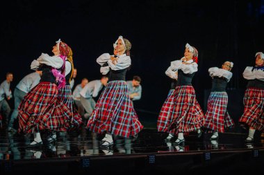 Valmiera, Letonya - 7 Haziran 2025 - GAUJA 80 'deki geleneksel Letonya halk dansları kolajı, renkli kostümlü dansçıları gece aydınlatmalı bir sahnede sergiliyorlar..