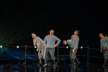 Valmiera, Letonya - 7 Haziran 2025 - GAUJA 80 'deki geleneksel Letonya halk dansları kolajı, renkli kostümlü dansçıları gece aydınlatmalı bir sahnede sergiliyorlar..