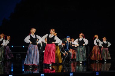 Valmiera, Letonya - 7 Haziran 2025 - GAUJA 80 'deki geleneksel Letonya halk dansları kolajı, renkli kostümlü dansçıları gece aydınlatmalı bir sahnede sergiliyorlar..